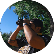 Person using binoculars in a green forested area.